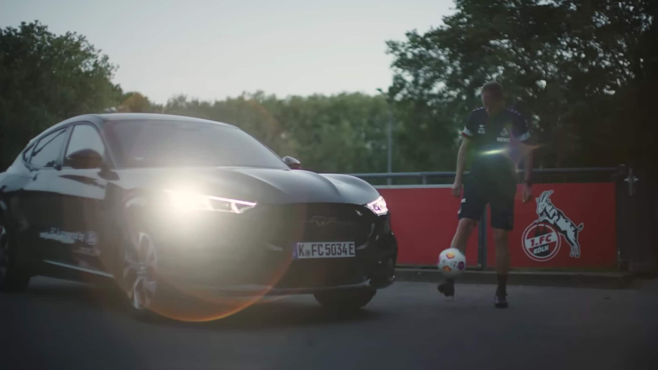 Man kicking a football in front of Mustang Mach E