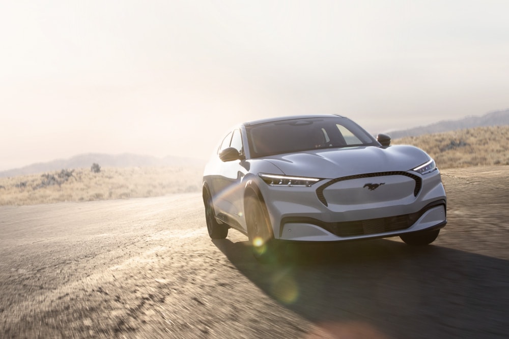 Um Ford Mustang Mach-E GT elétrico prateado dirigindo ao longo de uma estrada cênica.