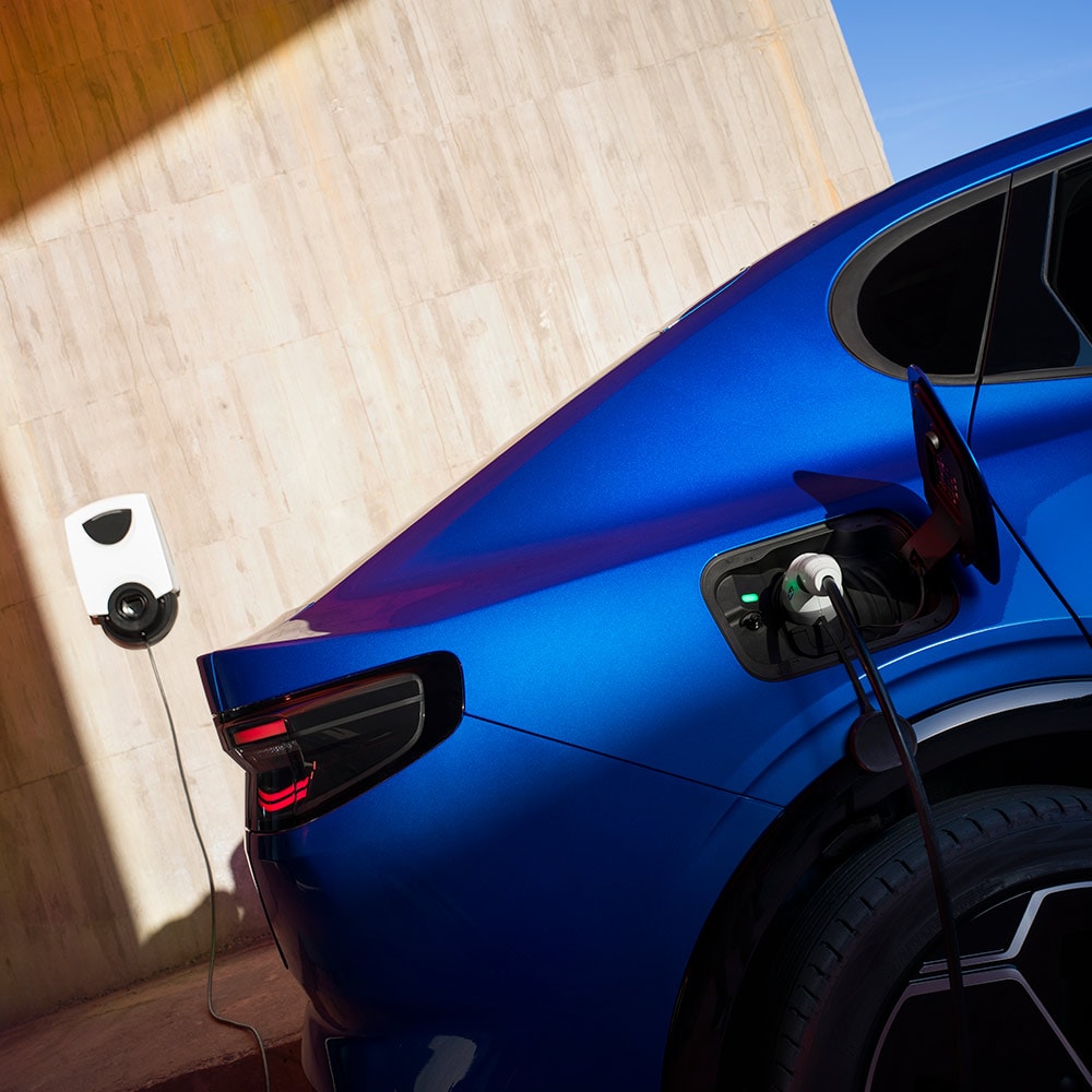 Vista traseira de um veículo elétrico Ford Capri azul conectado a um ponto de carregamento doméstico de veículos elétricos.