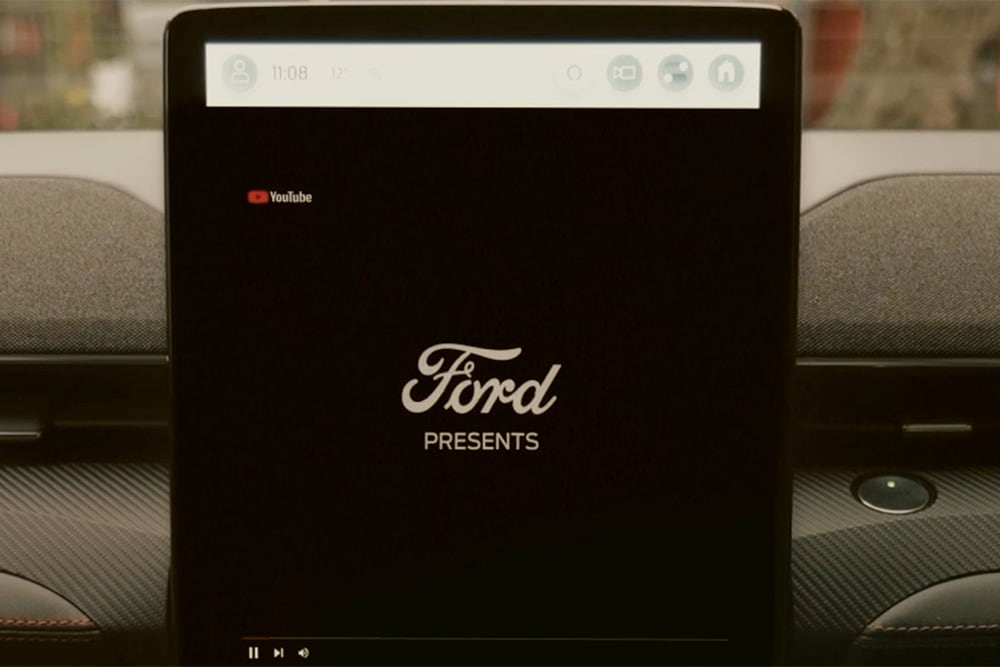 Grande plano do ecrã tátil SYNC 4 de 15,5" com a imagem "Ford apresenta", demonstrando a transmissão de vídeo no automóvel