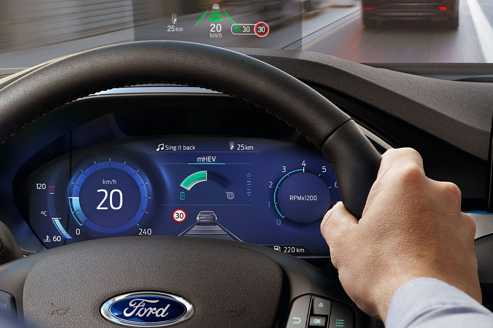 Mão a segurar um volante com um pequeno monitor acima do painel de instrumentos
