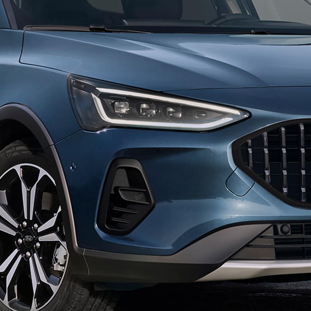 Close-up da frente de um Ford Focus Ative azul escuro, mostrando os faróis, grade e rodas de liga leve.