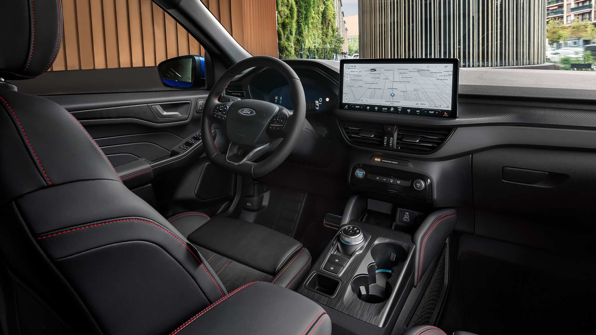 Interior do Ford Kuga mostra o volante com logótipo Ford, ecrã tátil grande SYNC® 4 e bancos pretos com pespontos vermelhos.