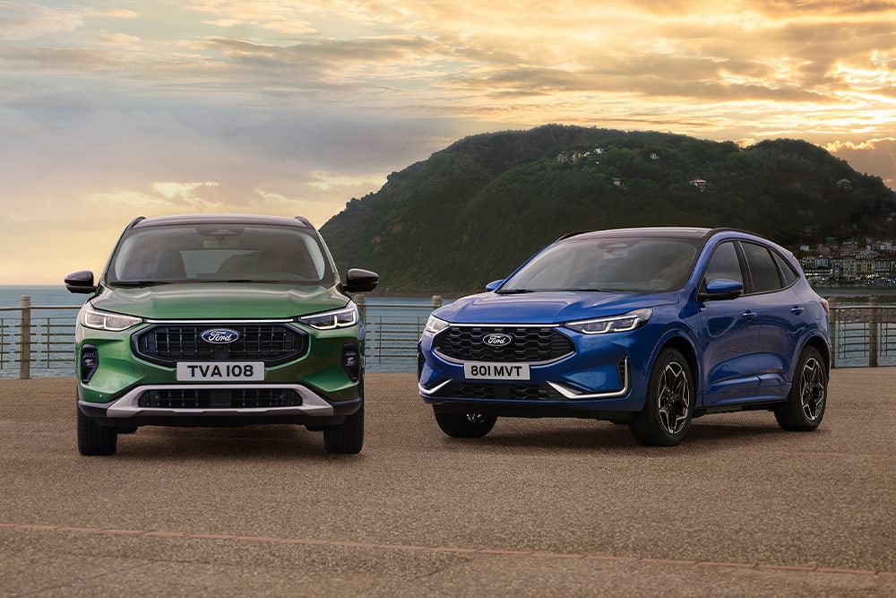 Um Ford Kuga Active verde e um Ford Kuga ST Line azul estacionados lado a lado num parque de estacionamento junto à costa.