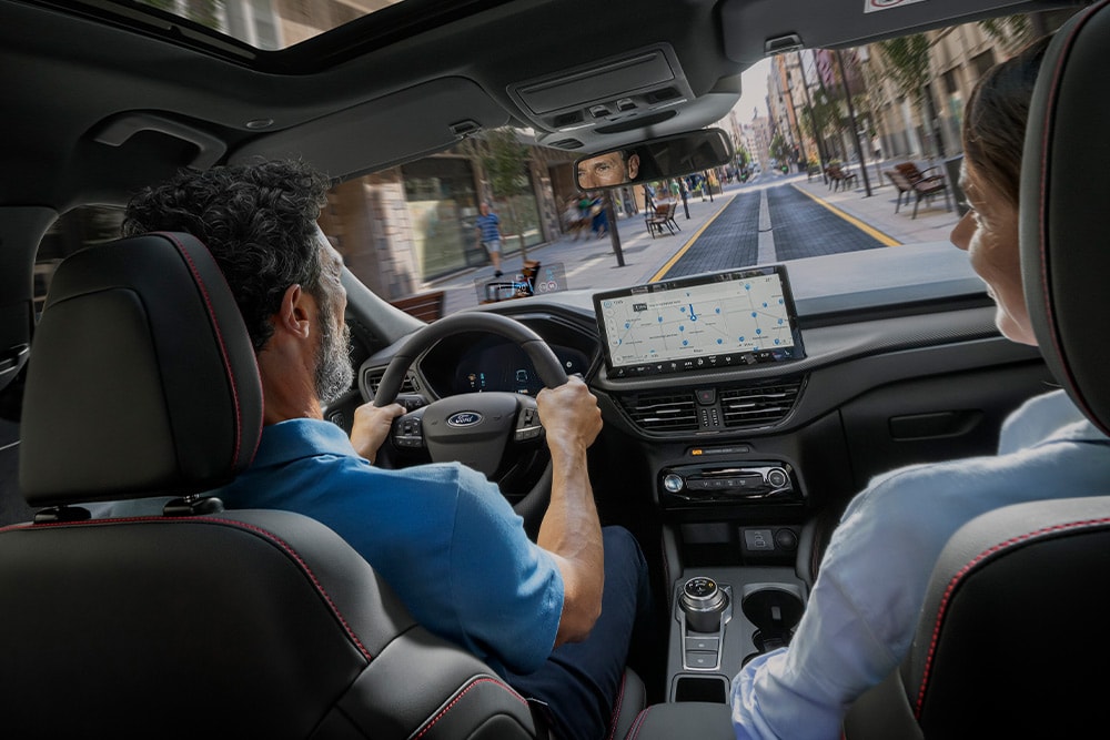Duas pessoas num Ford Kuga a conduzir numa rua da cidade a usar as instruções do ecrã digital de 12,3".