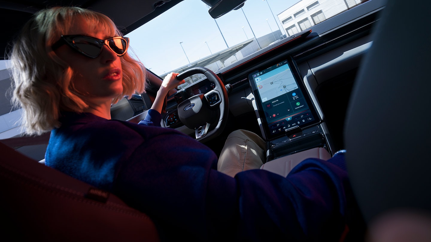 Woman driving the new Ford Capri® with view of the steering wheel, dashboard and large SYNC® Move touchscreen.