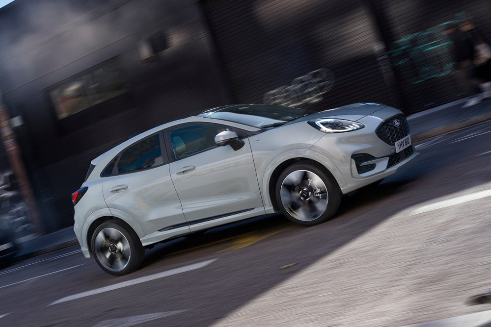 Ford Puma prateado da gama de carros pequenos da Ford a percorrer uma rua urbana.